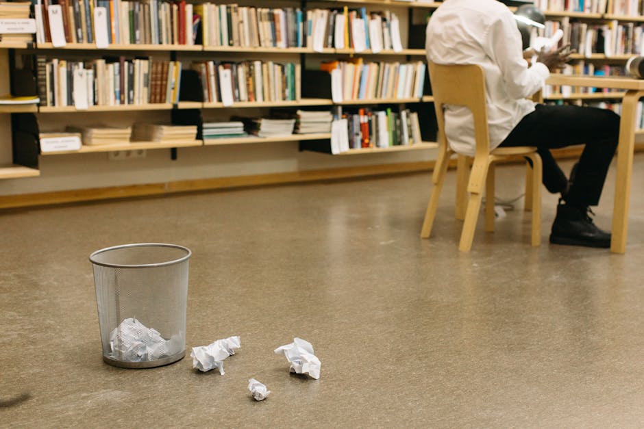 A library scene with crumpled papers near a trash can and a seated person, creating a thoughtful atmosphere.